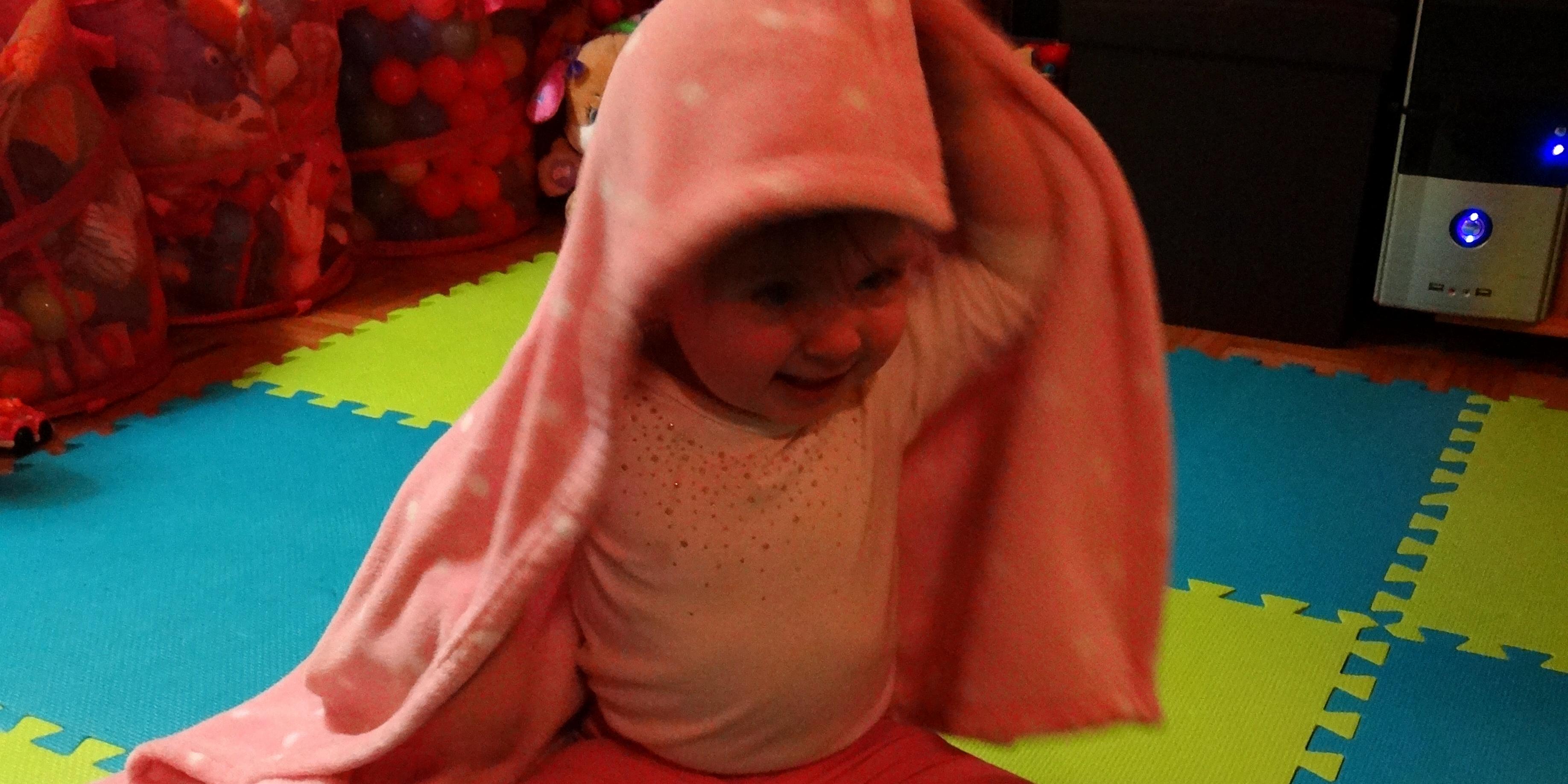 Baby girl playing Peekaboo with her pink blanket